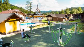 A hotel with outdoor exercise equipment, a pool, and a mountain backdrop.