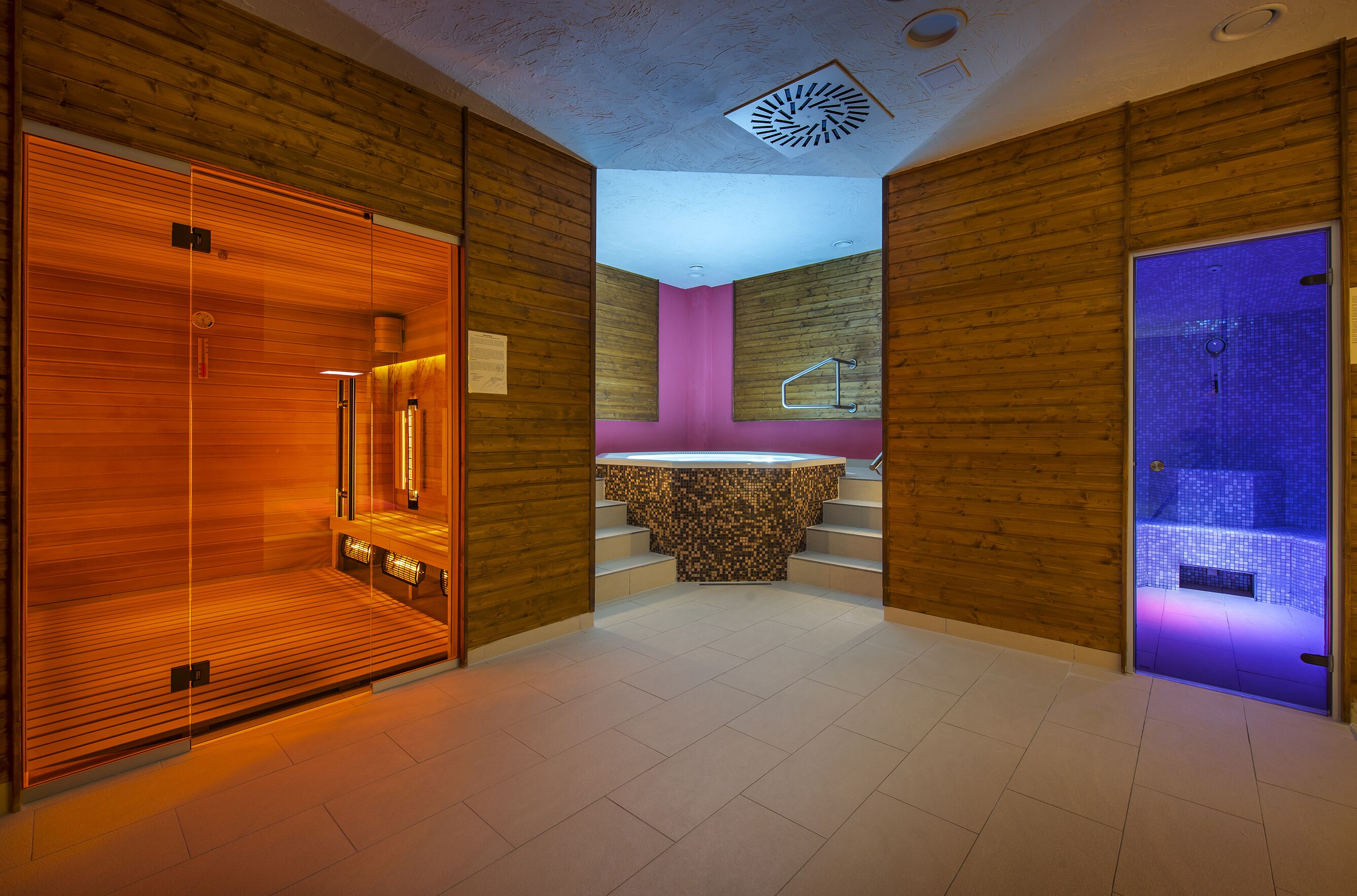 A modern bathroom with wooden paneling, a pink accent wall, and a blue-lit shower area.
