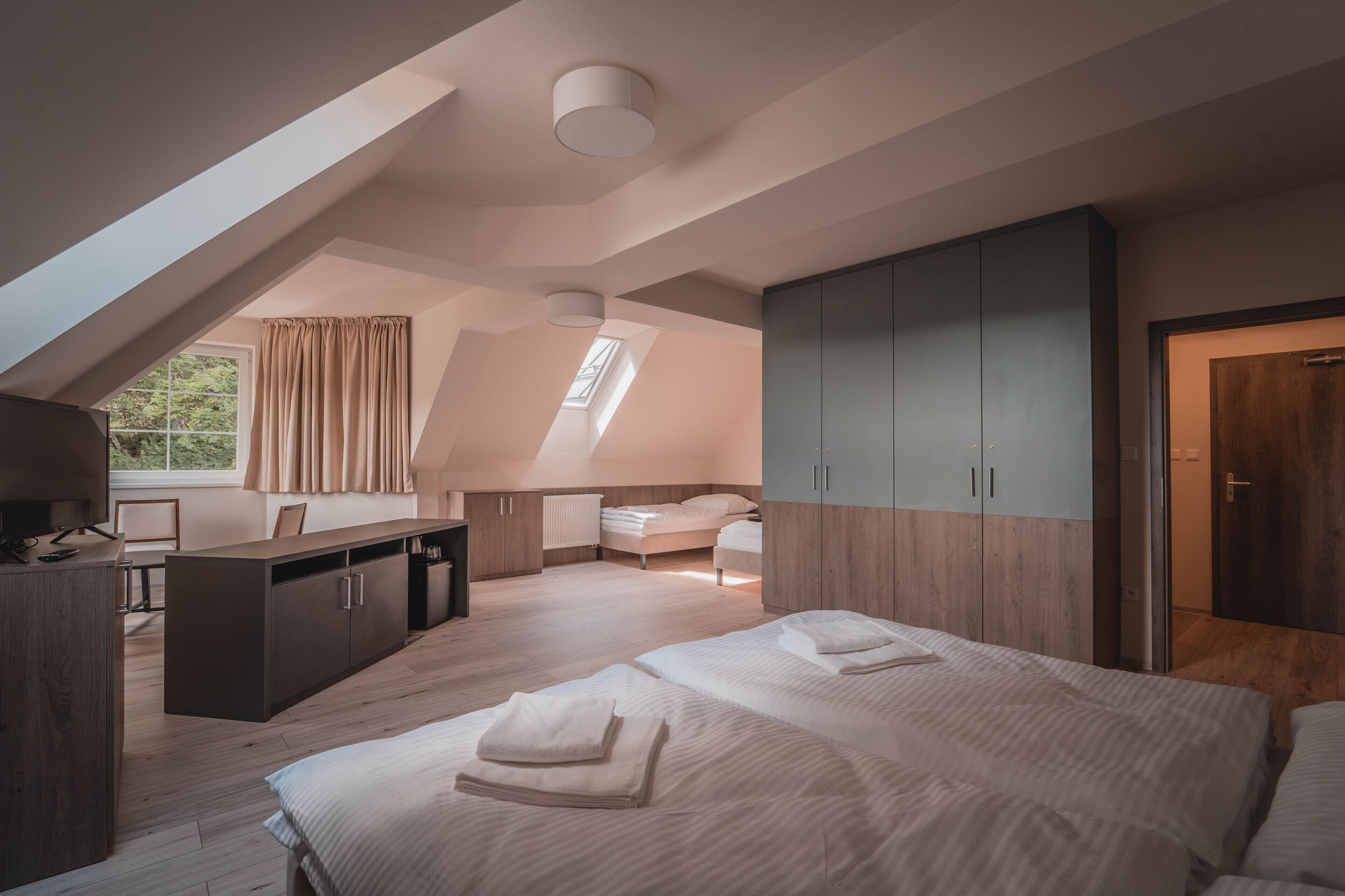 A modern, well-lit room with a large bed, a desk, and a wardrobe.