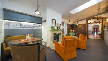 A hotel lobby with a dining area, seating, a fireplace, and a view of the outside.