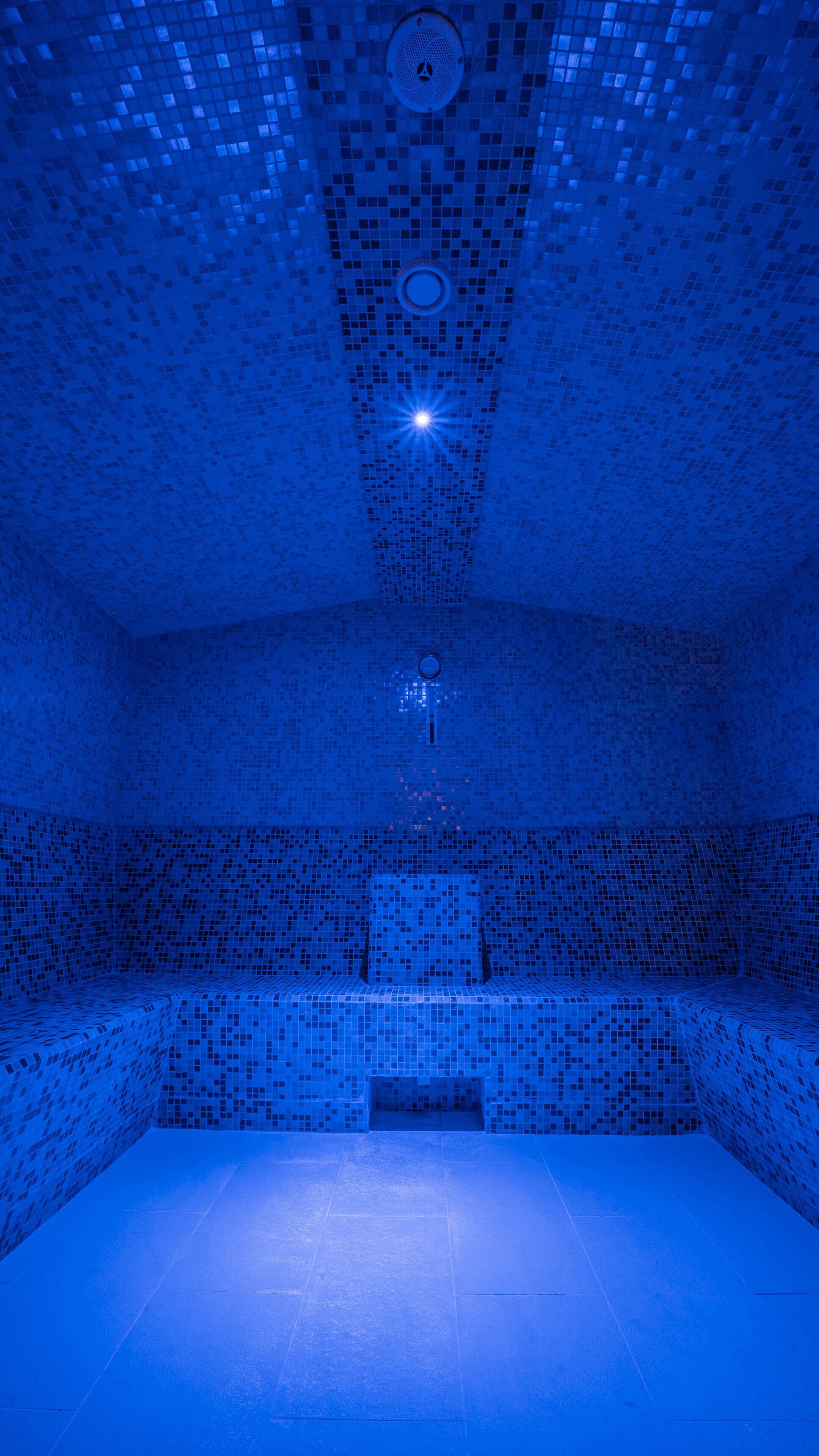 A blue-tiled room with a central light fixture, a bench, and a small opening at the back.