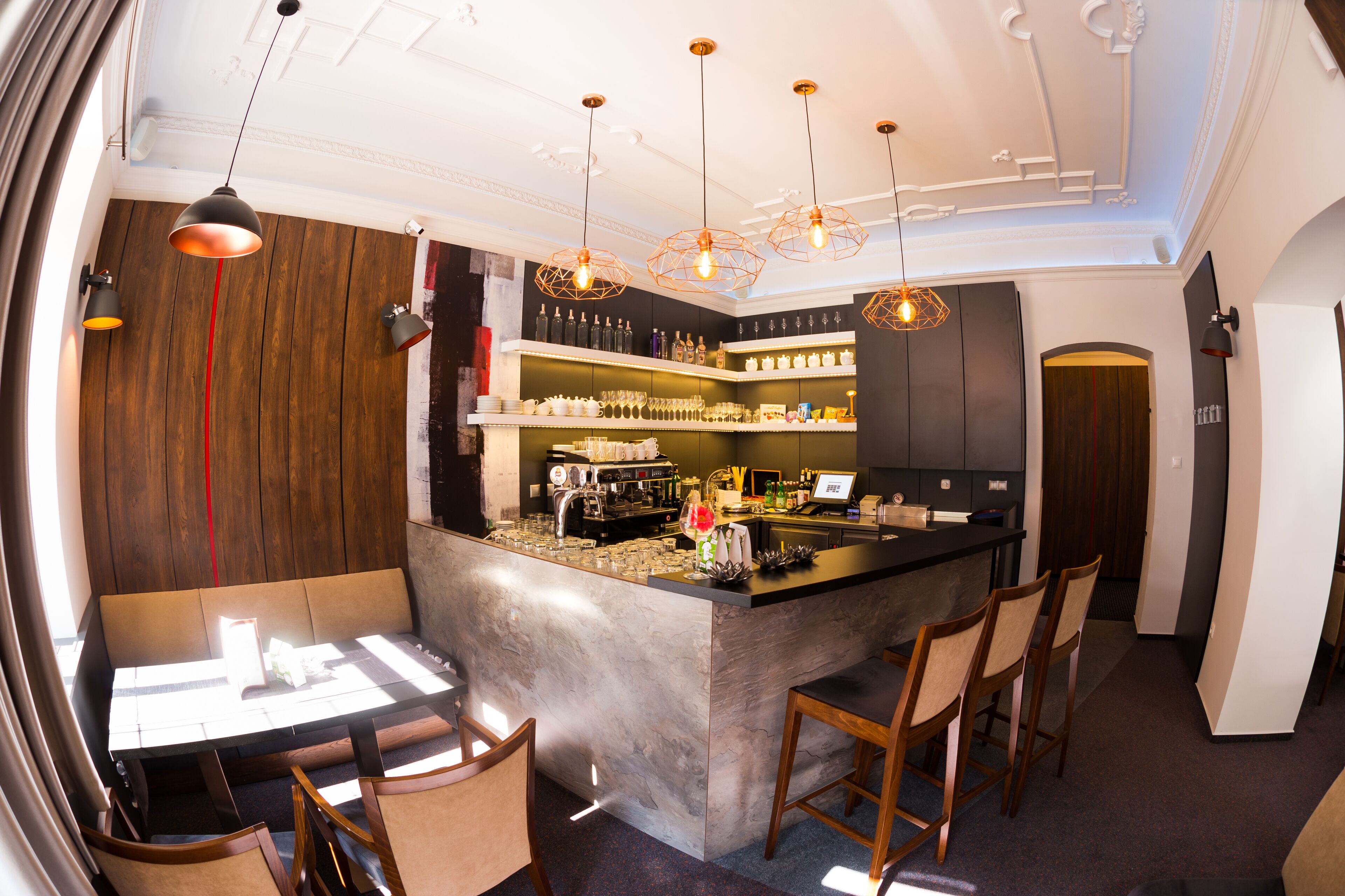 Un espace bar doté d’un comptoir en marbre, de chaises en bois et de luminaires suspendus.