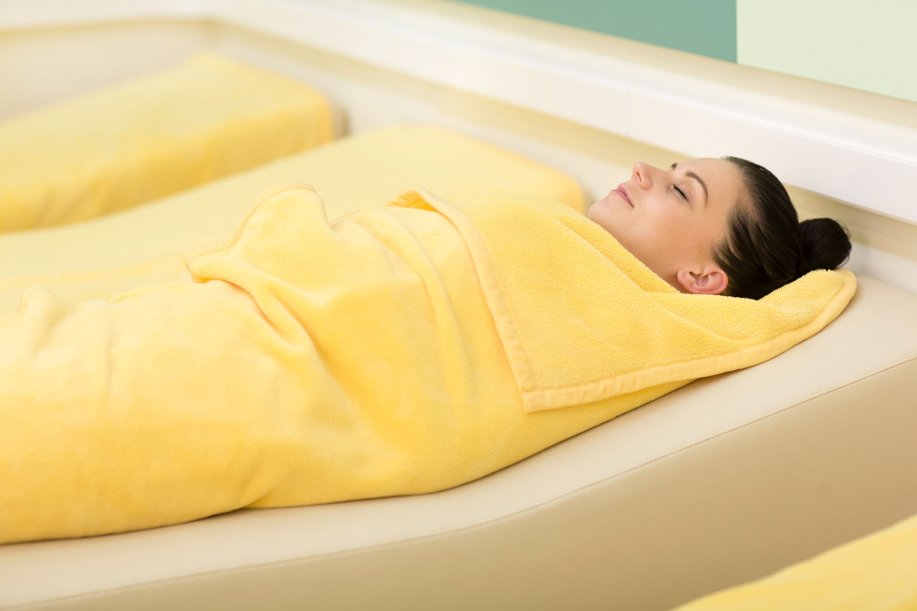 Une personne allongée sur un fauteuil de spa, recouverte d’une serviette jaune.