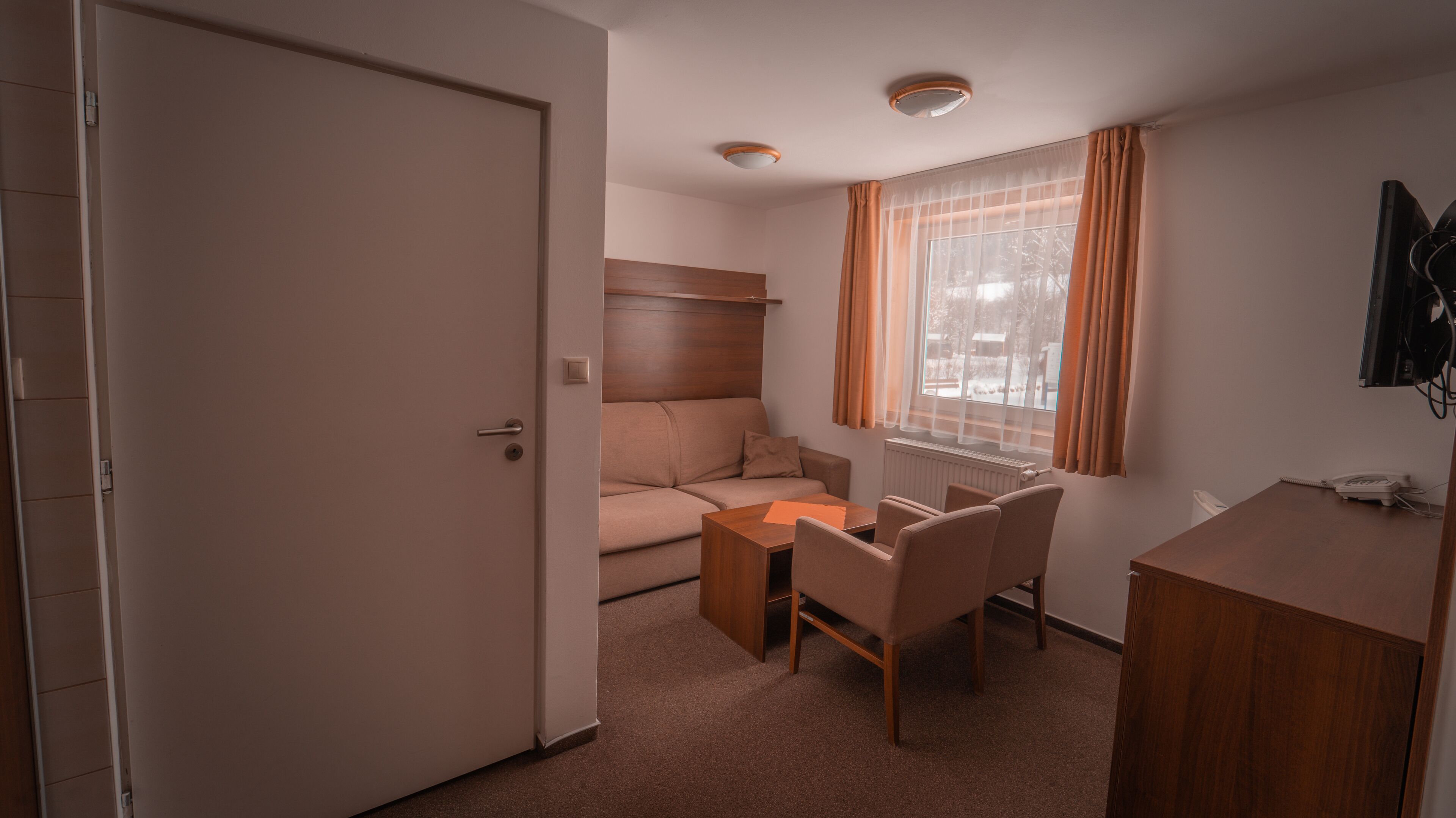 Une petite pièce comprenant un lit, un bureau, une chaise et une fenêtre avec des rideaux.