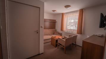 Une petite pièce comprenant un lit, un bureau, une chaise et une fenêtre avec des rideaux.