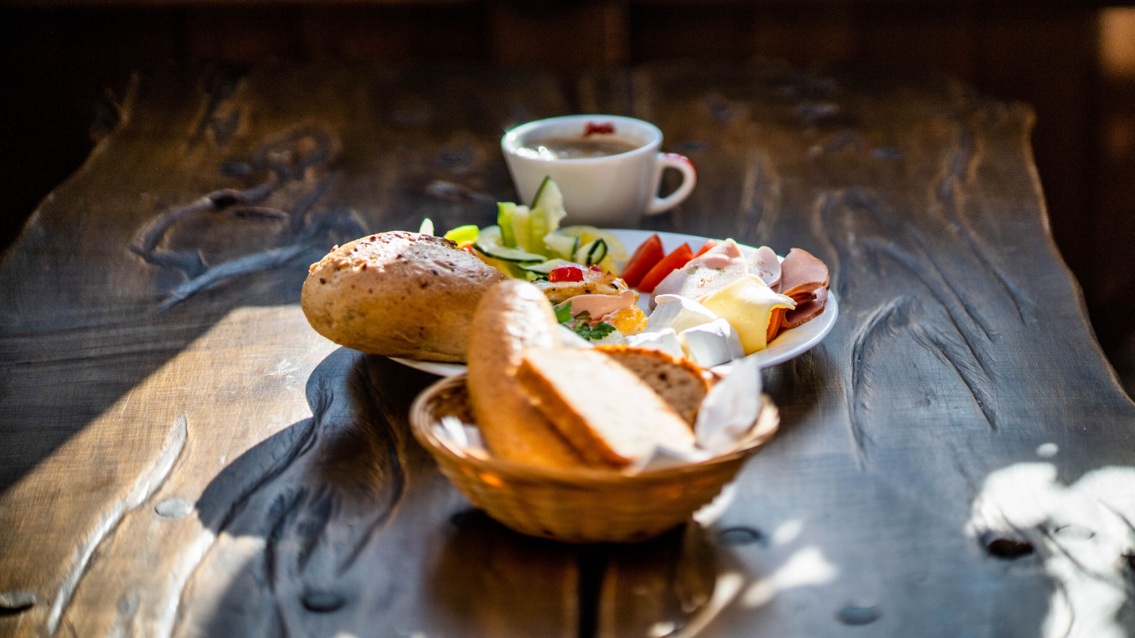 Une table en bois avec une assiette de nourriture, un panier et une tasse de café.