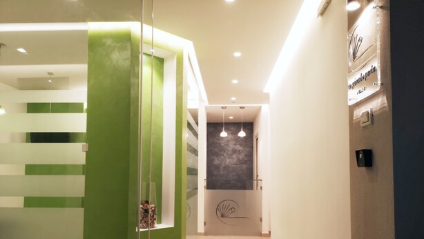 A modern hotel lobby with a green accent wall, a glass partition, and a staircase leading to an upper level.