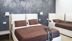 A modern hotel room with two beds, each with a white headboard and brown bedding. There are wall-mounted lamps on either side of the beds.