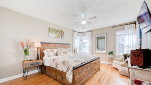 A bedroom with a wooden bed, a nightstand, a ceiling fan, and a window with curtains. - Copacabana - Waves of Fun! (Lubbock)
