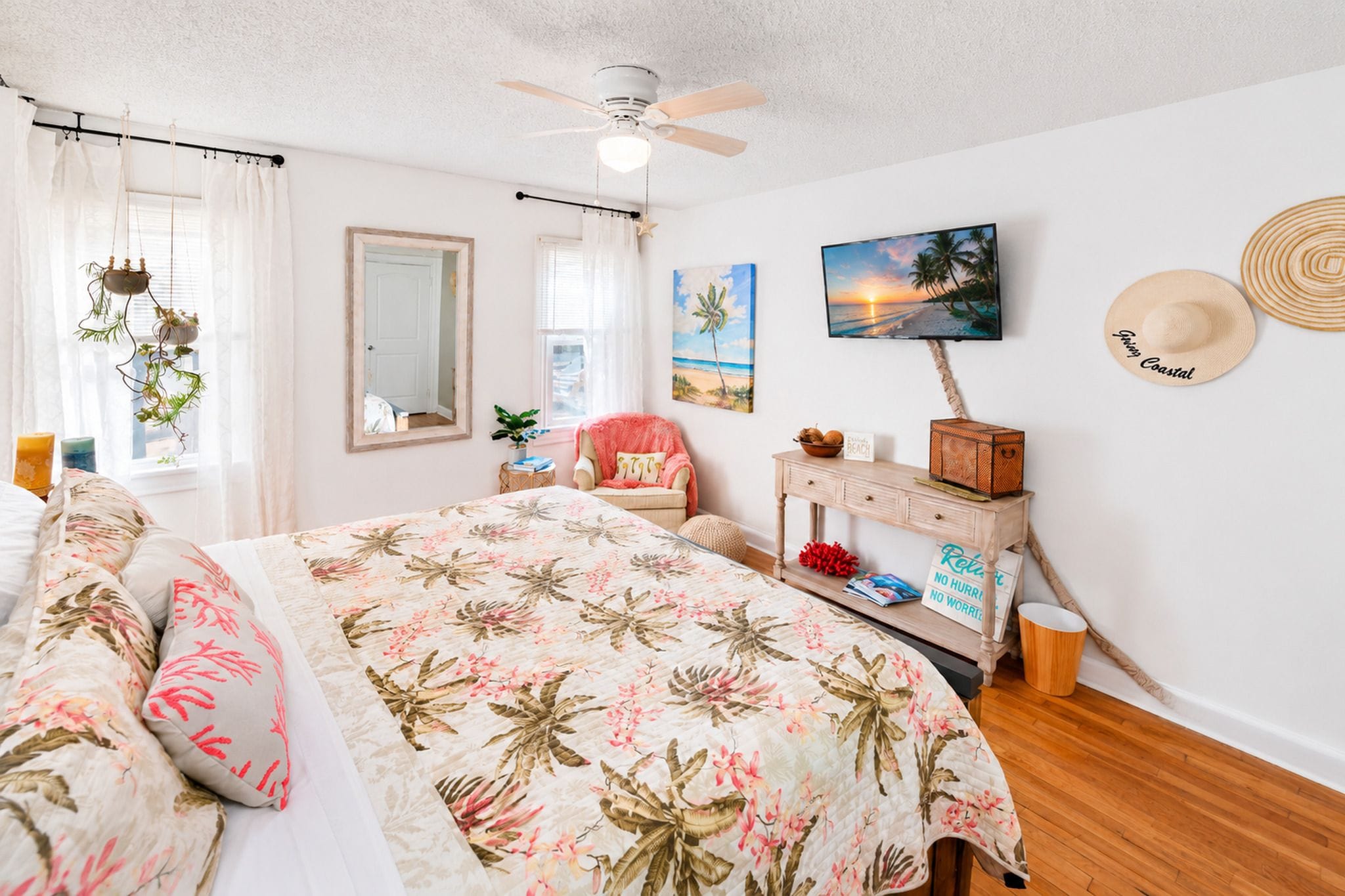 Une chambre à coucher comprenant un lit, une chaise, une commode, un miroir, un ventilateur de plafond et un téléviseur fixé au mur.