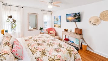 Une chambre à coucher comprenant un lit, une chaise, une commode, un miroir, un ventilateur de plafond et un téléviseur fixé au mur.