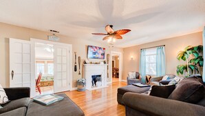 A spacious living room with a fireplace, a ceiling fan, and a television. - Copacabana - Waves of Fun! (Lubbock)