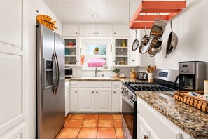 A modern kitchen with white cabinetry, a stainless steel refrigerator, a gas stove, and a coffee maker.