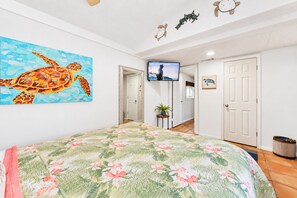 Une chambre avec un grand lit, un téléviseur fixé au mur et un tableau représentant une tortue de mer.