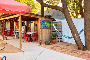 An outdoor patio area with red chairs and tables, a wooden structure with a colorful mural, and a hammock.