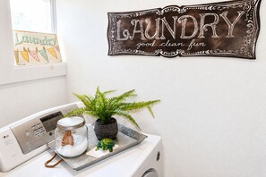 Un espace dédié à la lessive, comprenant un lave-linge, un étendoir, un pot de lessive et une plante en pot.