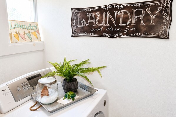 A laundry area with a washing machine, a drying rack, a jar of detergent, and a potted plant.