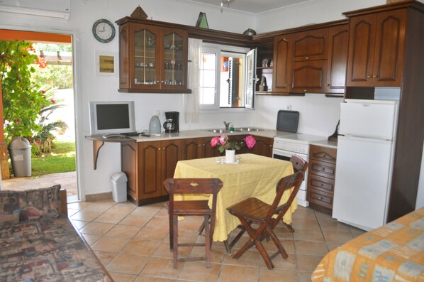 A kitchen with wooden cabinets, a dining table with chairs, a refrigerator, and a window with curtains.