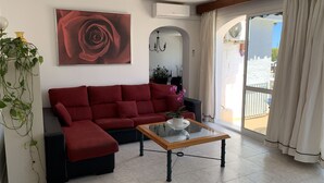 A living room with a red sofa, a glass coffee table, and a large window with curtains. - Casa Playa El Torreon (La cala de mijas)
