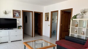 A living room with a TV, sofa, and coffee table. There are doors leading to other rooms. - Casa Playa El Torreon (La cala de mijas)