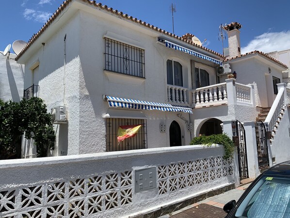 Um edifício de dois andares com fachada branca, uma varanda com toldo azul e branco listrado e uma bandeira hasteada na frente.