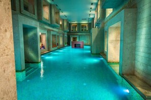 Une longue et Ă©troite piscine intĂ©rieure, avec une cheminĂ©e centrale, entourĂ©e de murs en pierre et dotĂ©e de nombreuses fenĂȘtres.