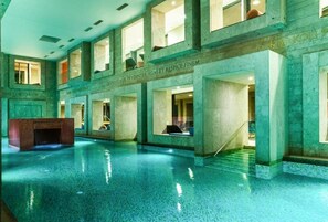 A large indoor swimming pool with clear water, surrounded by stone walls and multiple windows. - Hotel Rimski Dvor - Rimske Terme (Lasko)