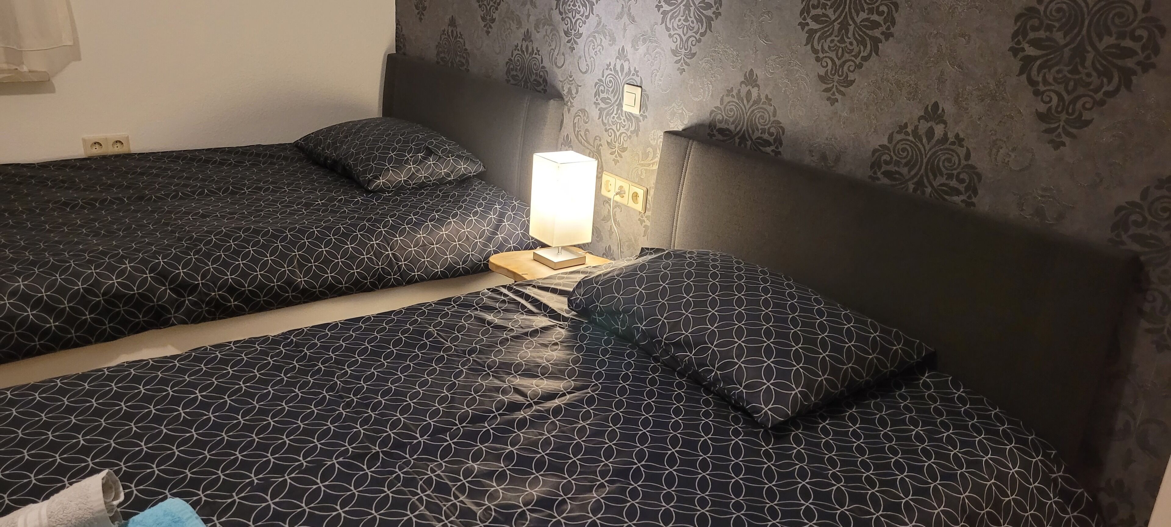 Una habitación con dos camas, cada una con una colcha de diseño geométrico y almohadas a juego. Hay una mesita de noche con una lámpara entre las camas.