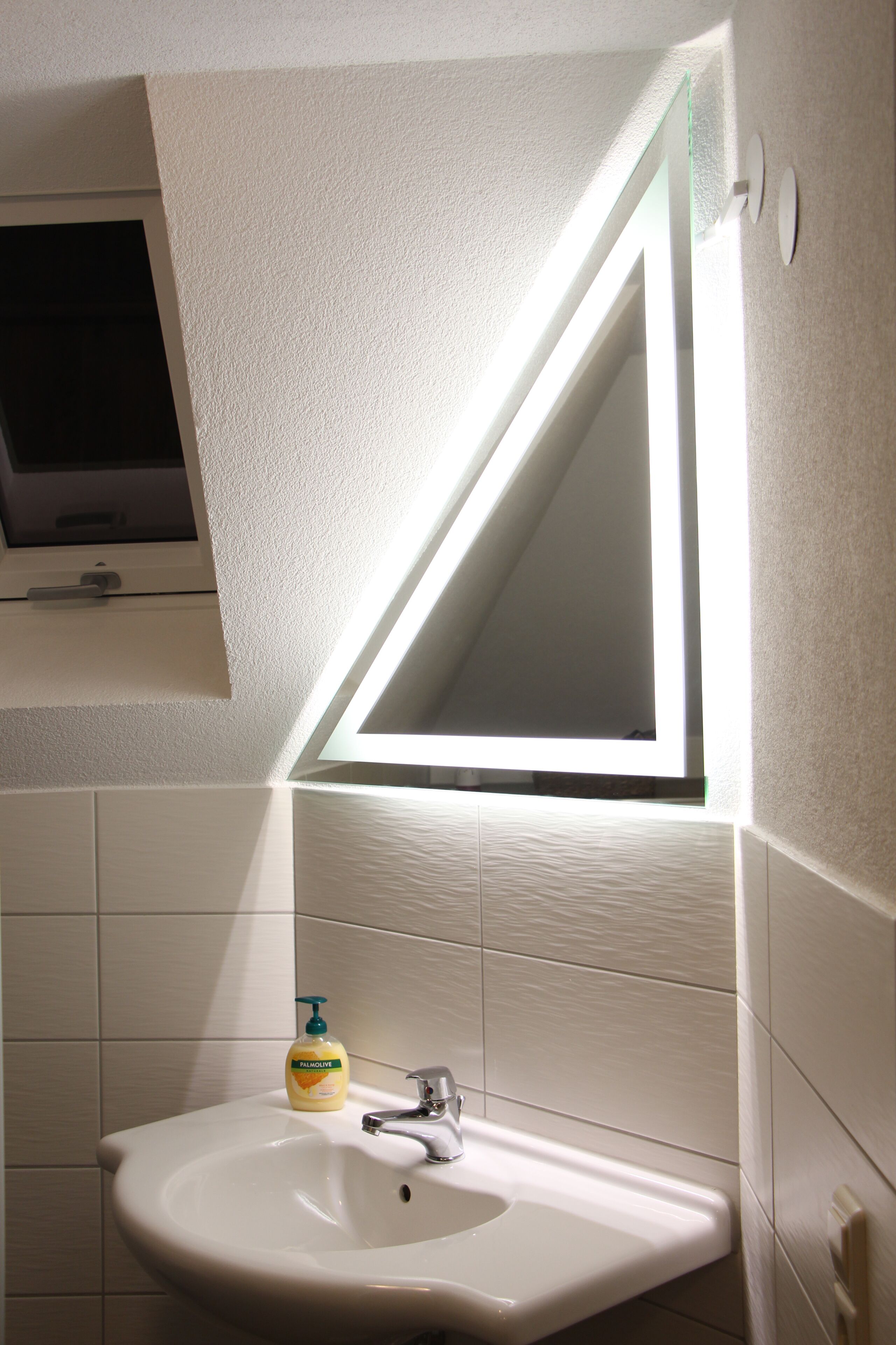 A bathroom with a white sink, a mirror, and a window above the mirror.