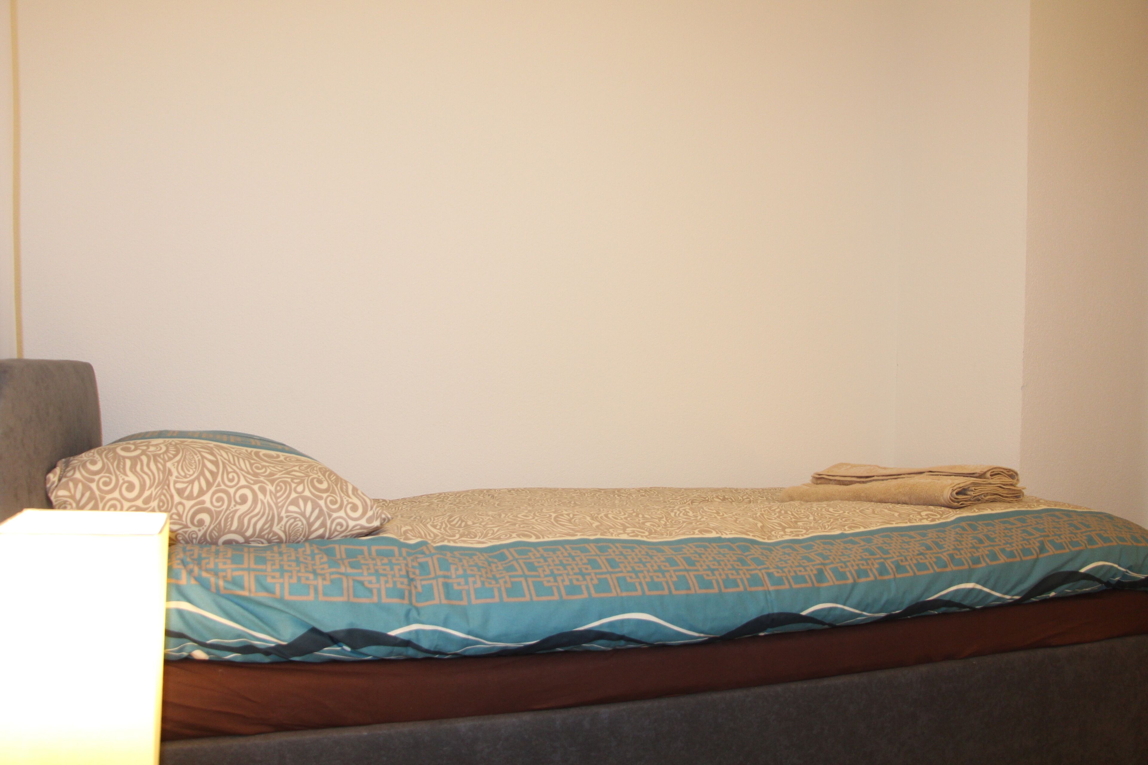 A neatly made bed with patterned bedding and a folded towel on top.