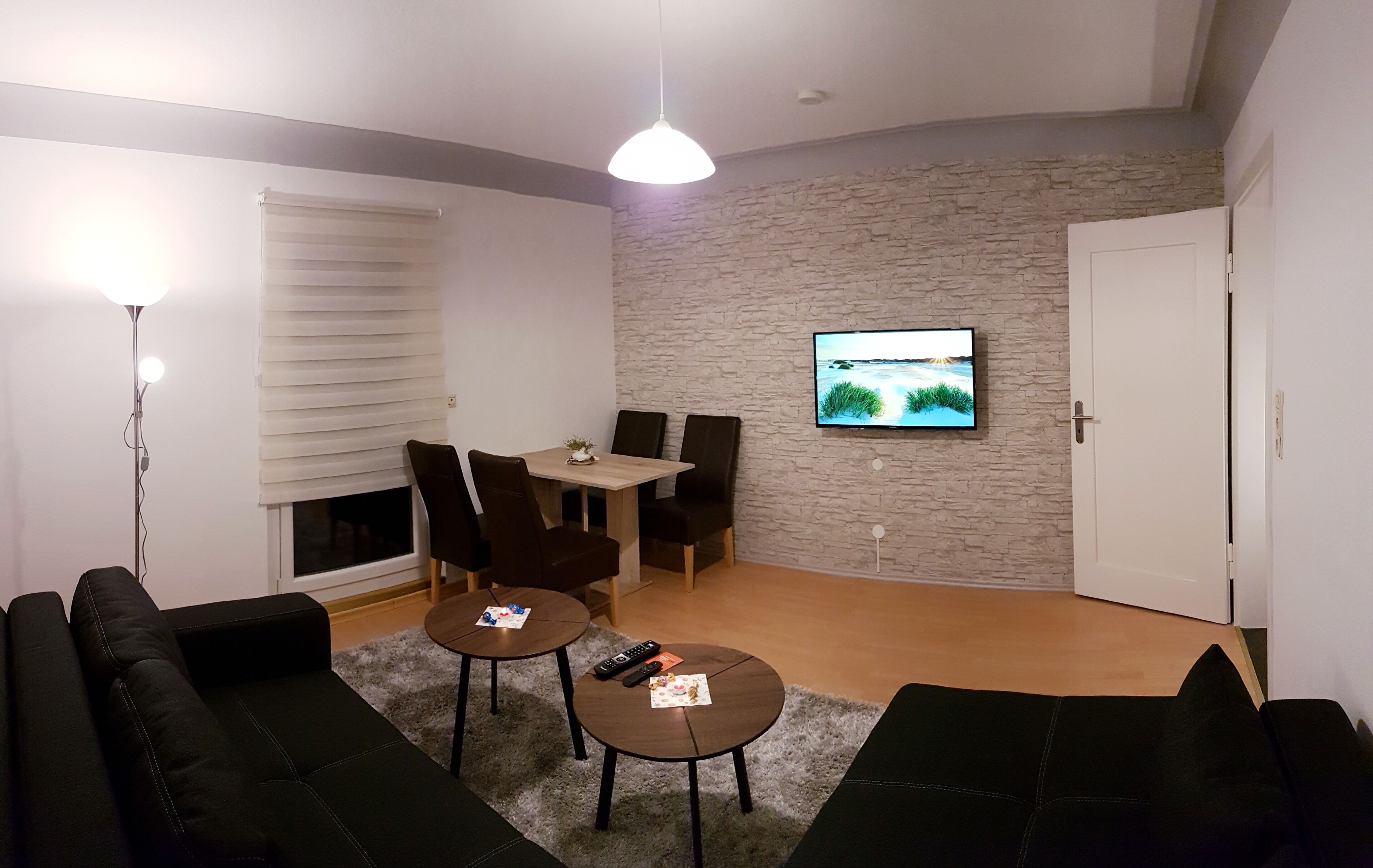 Ein Wohnzimmer mit Kamin, einem an einer Steinwand befestigten Fernseher, einem Essbereich mit Stühlen und einem schwarzen Ledersofa.