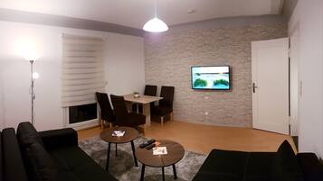 Ein Wohnzimmer mit Kamin, einem an einer Steinwand befestigten Fernseher, einem Essbereich mit Stühlen und einem schwarzen Ledersofa.