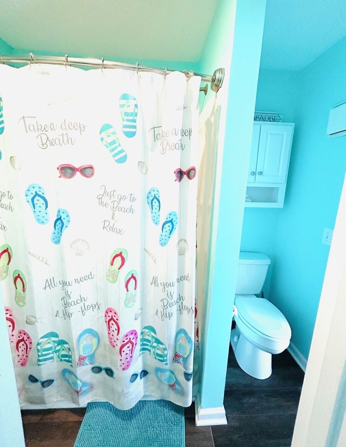 Une salle de bain équipée d’un rideau de douche orné de motifs sur le thème de la plage, de toilettes et d’un meuble de rangement.