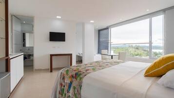 Un dormitorio con cama, televisor montado en la pared, ventana con vistas y un baño al fondo.