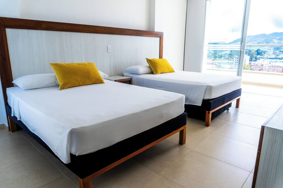 Two single beds with wooden frames and white bedding, a wooden headboard, and a view of a cityscape through a large window.