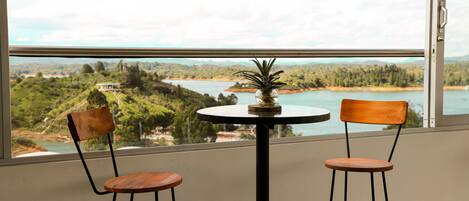 Una habitación con dos sillas de madera y una pequeña mesa, una ventana con vista a un lago y vegetación.