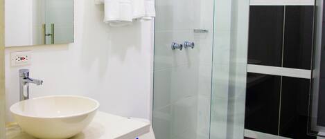 Een moderne badkamer met een douchecabine van glas, een witte wastafel en een toilet.