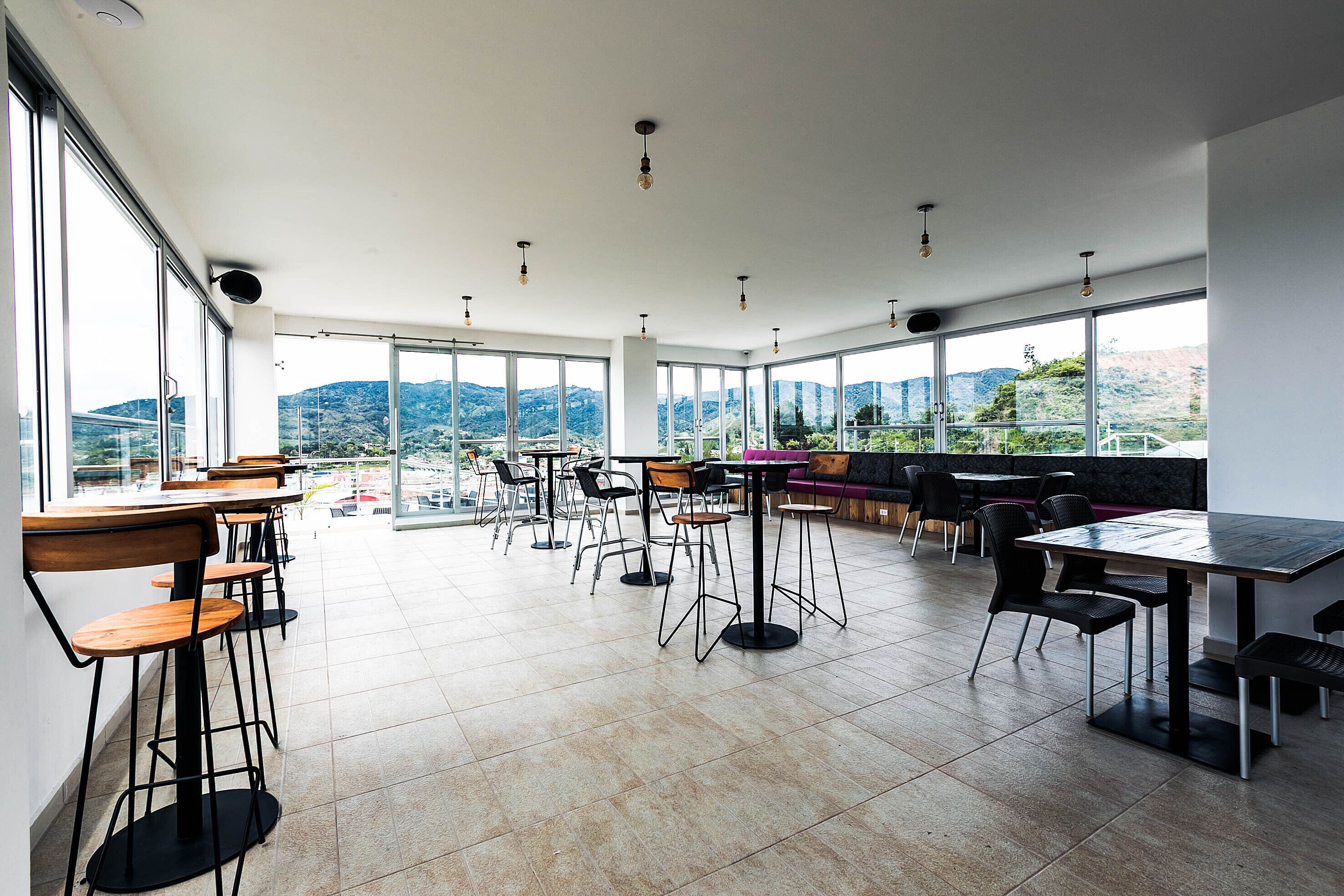 A modern dining area with high tables and chairs, large windows offering mountain views, and a clean, minimalist design.