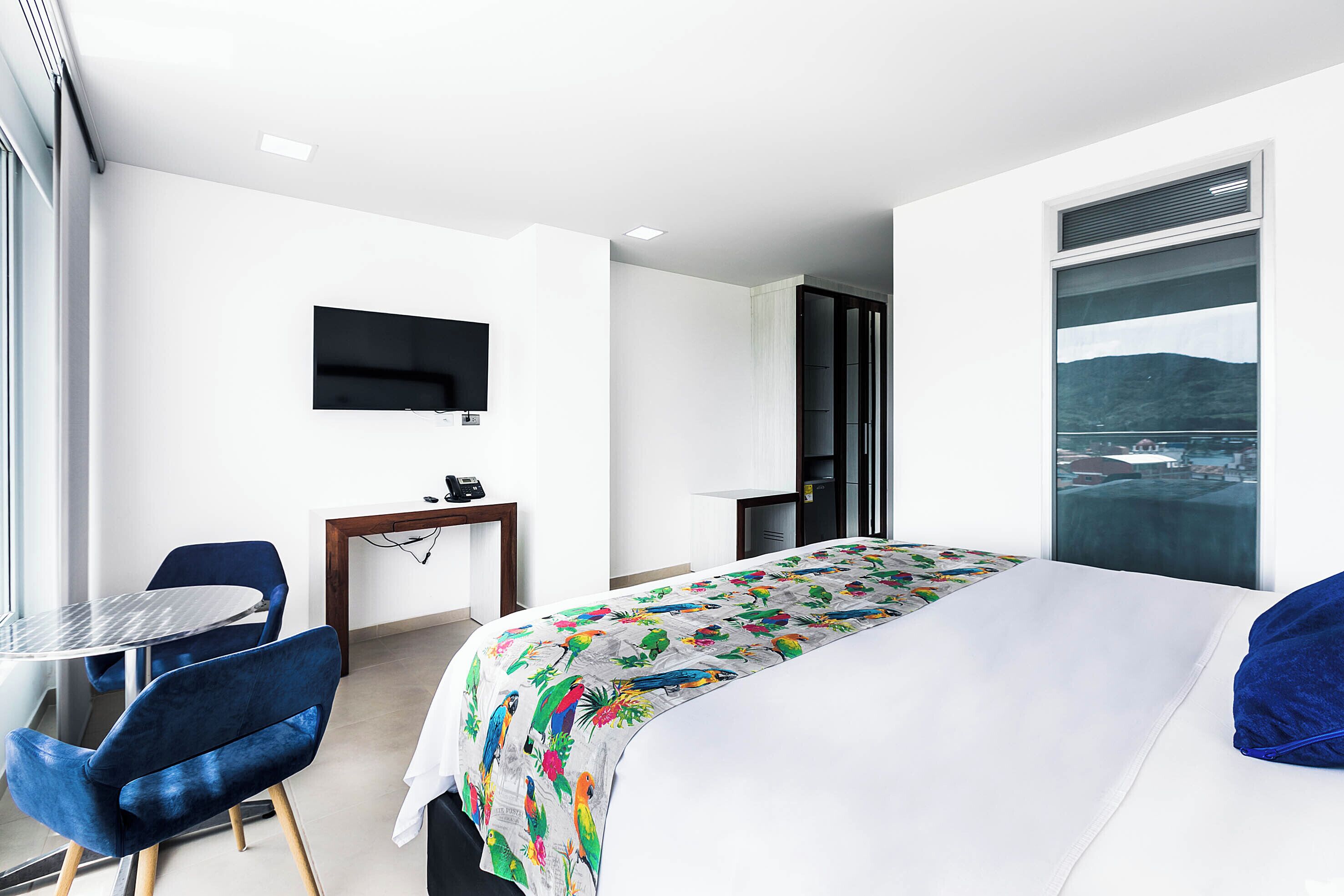 A modern hotel room with a bed, a desk, a chair, a TV, and a window with a city view.