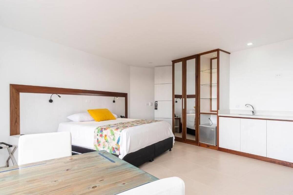 A hotel room with a bed, a desk, a chair, a wardrobe, and a kitchenette.