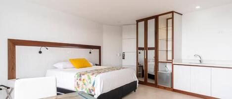 Una habitación de hotel con cama, escritorio, silla, armario y kitchenette.