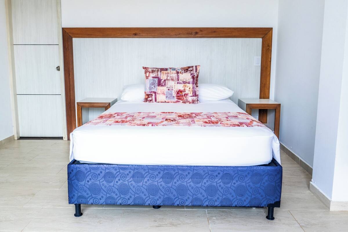 A bed with a blue patterned bedspread, a wooden headboard, and a decorative pillow.