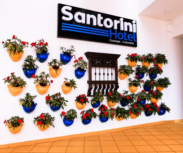 A wall with a sign for Santorini Hotel in Guatemala, Colombia, and multiple potted plants arranged in a pattern. - Hotel Santorini (Guatapé)