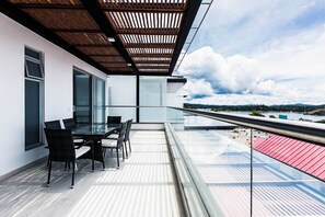 A balcony with a glass railing, a dining table with chairs, and a view of a red-roofed building across the street. - Hotel Santorini (Guatapé)