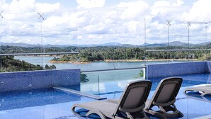 An infinity pool with two lounge chairs and a view of a lake and mountains. - Hotel Santorini (Guatapé)