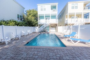 A swimming pool with lounge chairs, a white fence, and a two-story building with balconies. - FADE AWAY -New 5 Bedroom House Only Steps From The Ocean With a Private Pool (Surfside Beach)