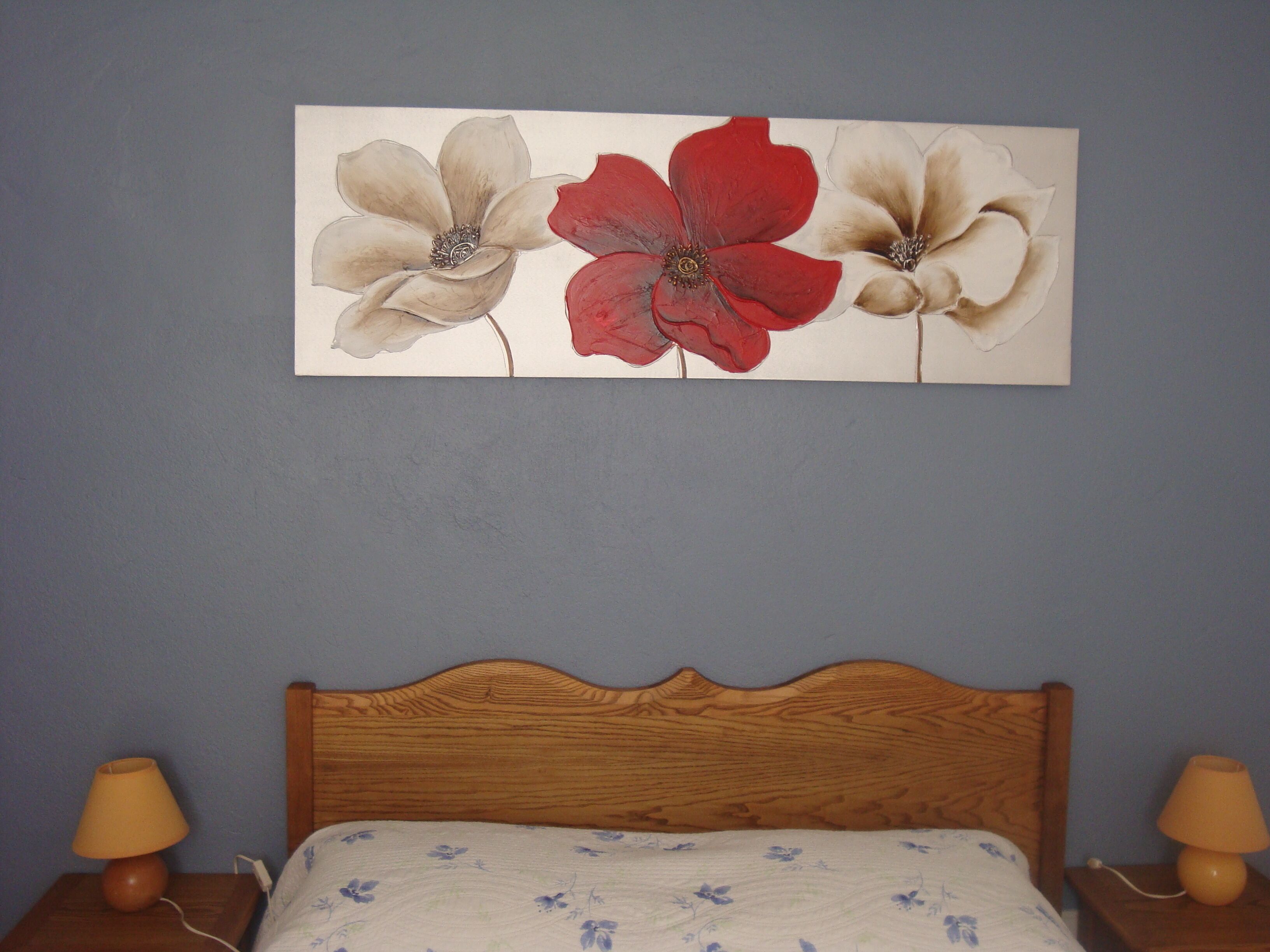 Une chambre à coucher avec une tête de lit en bois, un lit recouvert d’une couvre-lit à motifs floraux et un tableau représentant trois fleurs, accroché au mur.