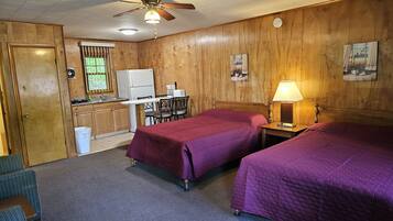 Une chambre d’hôtel avec deux lits, un coin cuisine, un ventilateur de plafond et une horloge au mur.
