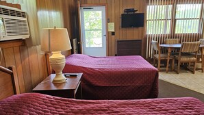 Een hotelkamer met twee bedden, een televisie, een lamp, een eettafel met stoelen en uitzicht op de omgeving.