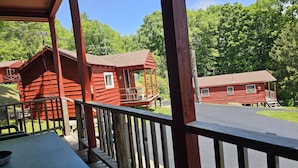 Een rode houten chalet met een balkon, omringd door weelderige begroeiing en een heldere lucht.